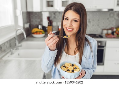 Close-up Of Smiling Young Woman Eating Breakfast Cereals Of Bowl At Home.