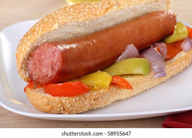 Closeup Of A Smoked Sausage On A Sesame Seed Bun With Fried Peppers And Onions