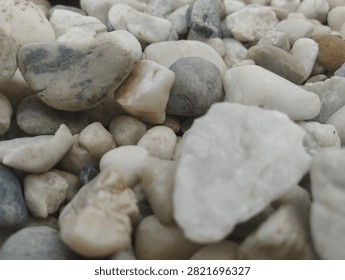 Close-up of smooth rounded pebbles and river stones in white, gray, and beige shades. Natural rock textures, varied shapes, earthy tones, perfect for background or decorative material.