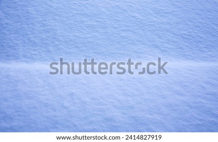 A close-up of a smooth, unbroken expanse of snow, showcasing subtle textures and the gentle play of light and shadow in hues of blue