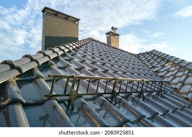 Closeup snow guard for safety in winter on house roof top covered with ceramic shingles. Tiled covering of building
