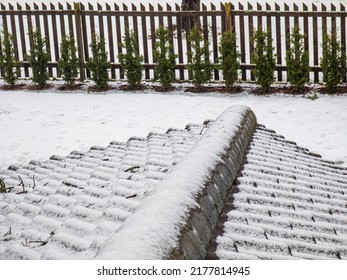 Close-up Of Snow On Roof Tiles. Winter Mood. Fence And Green Trees In Garden. Above View.