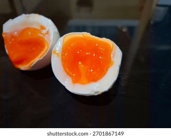 Close-up of a soft boiled egg cut in half showing the rich orange runny yolk and white egg shell on a dark reflective surface. Perfect for food and drink themes, breakfast concepts, protein diet ideas