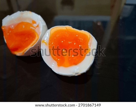 Close-up of a soft boiled egg cut in half showing the rich orange runny yolk and white egg shell on a dark reflective surface. Perfect for food and drink themes, breakfast concepts, protein diet ideas