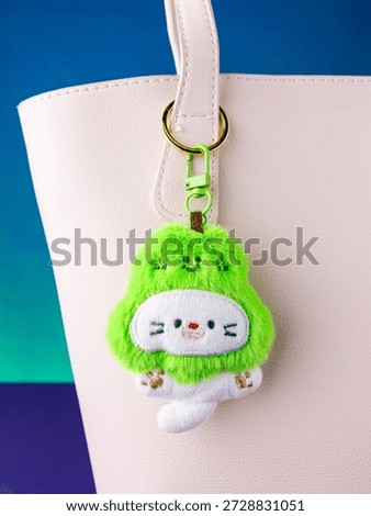 A close-up of a soft plush keychain featuring a cute and playful white kitten wearing a pear-shaped hat  on white bag