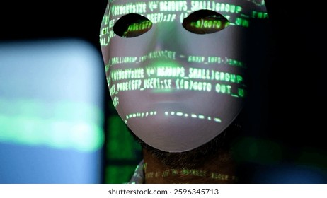 Close-up of a software developer with a masked face. Screen light and computer code reflected in his face. System administrator. Concept of cybersecurity and hacking.