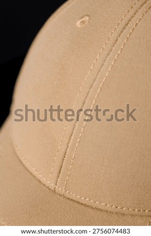 Close-up of a solid sand-colored baseball cap. Front view of a beige cap with a curved visor on a black surface