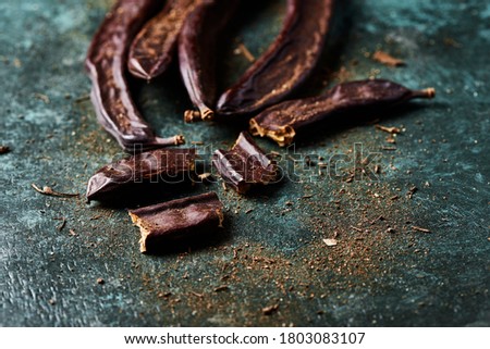 closeup of some ripe carob beans on a rustic dark green surface