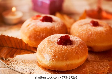 closeup of some sufganiyot, Jewish donuts filled with strawberry jelly traditionally eaten on Hanukkah, and some lit candles on a set table