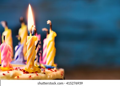 closeup of some unlit candles and just one lit candle after blowing out the cake