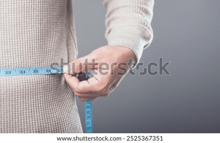 A close-up of someone using a blue measuring tape to measure their waist or hips, symbolizing the concept of maintaining a healthy body and preventing excessive weight gain