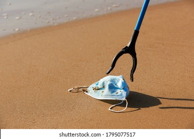 closeup of someone using a reach extender to collect a blue used surgical mask thrown on the wet sand of the seashore - Powered by Shutterstock