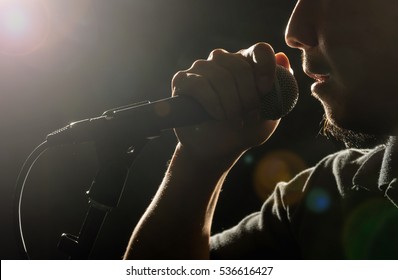 Closeup Songer Hand Holding The Microphone And Singing On Black Background With Lens Flare From Spot Light, Musical Concept