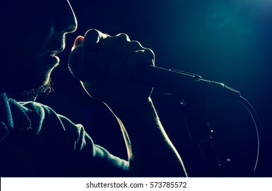 Closeup Songer Hand Holding The Microphone And Singing On Black Background With Lens Flare From Spot Light, Musical Concept