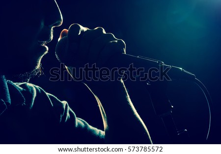 Closeup Songer hand holding the microphone and singing on black background with lens flare from spot light, musical concept