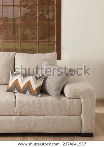 Close-up of Sophisticated Fabric Living Room Sofa, Weaved Neutral Fabric, Zigzag-Patterned Cushion in Blue, Brown, White, Muted Gray Pillow, Set Against Window with Brown Slatted Blinds, Creamy Wall.
