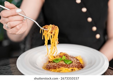 Close-up of spaghetti with breaded cutlet, basil, and cheese on a plate. A person in black with gold buttons lifts pasta with a fork. Italian cuisine, dining concept