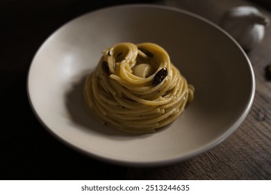 A close-up of spaghetti with garlic, olive oil, and chili peppers is elegantly plated. The warm tones and simple presentation highlight the rustic Italian dish on a wooden table. - Powered by Shutterstock