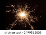 A close-up of a sparkler emitting bright sparks against a dark background.