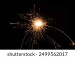 A close-up of a sparkler emitting bright sparks against a dark background.