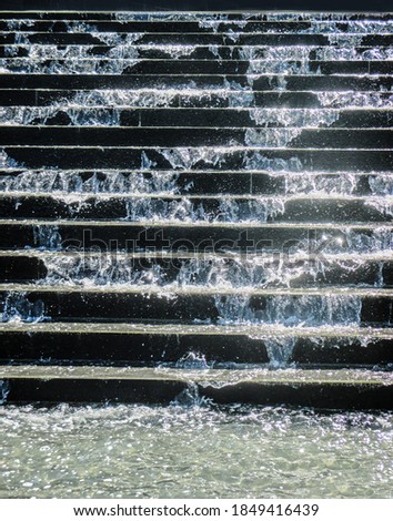 Close-up of sparkling water spashing down concrete stairs in a fountain into pool below  with water drops in the air                  