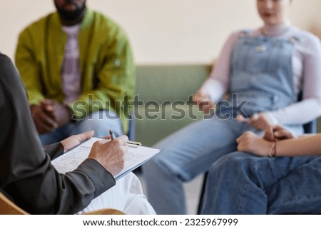 Close-up of specialist making notes in document while talking to people at psycho session