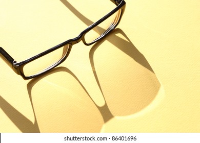 Closeup of spectacles with long shadow on yellow surface