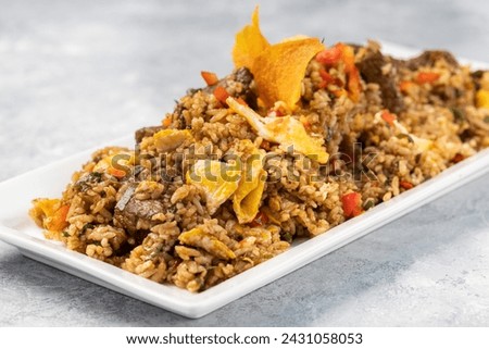 A closeup of spicy cooked rice with meat, vegetables and chips in a plate on the table