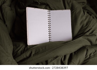 close-up of a spiral notebook opened with lined pages blank on a dark green comfy blanket in natural lighting in a horizontal orientation