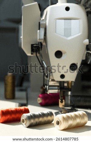 Close-up of spools of metallic colour threads laying on the white table in front of industrial sewing machine. Sewing tools for professional dress maker or for hobby sewing