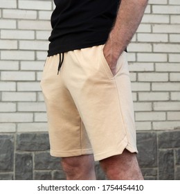 Close-up Sports Men’s Sand-colored Shorts On A Man Against A White Brick Wall, Square Photo