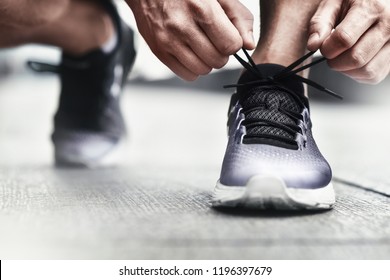 Close-up Of Sportsman Tying Sneakers. Unrecognizable Man Stopping Lacing Shoe Outdoors. Athletic Shoes Concept. Color Version