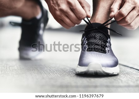 Close-up of sportsman tying sneakers. Unrecognizable man stopping lacing shoe outdoors. Athletic shoes concept. Color Version