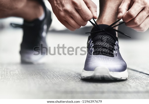 Close-up of sportsman tying sneakers.\
Unrecognizable man stopping lacing shoe outdoors. Athletic shoes\
concept. Color Version