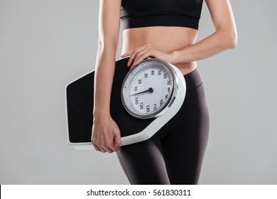 Closeup of sportswoman standing and holding weighing scale over gray background