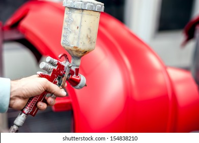 Close-up Of Spray Gun With Red Paint Painting A Car In Special Booth