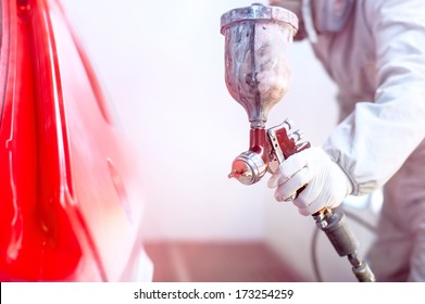 Close-up of spray gun with red paint painting a car in special booth