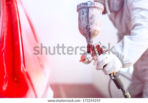 Close-up of spray gun with red paint painting a car
in special booth
