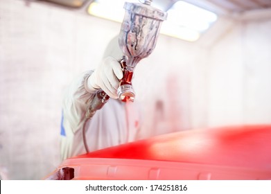 Close-up of spray gun and worker painting a car