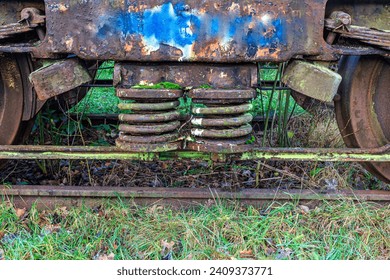 Close-up of springs of secondary shock absorber between two railway wheels of bogie, very old, damaged, worn and corroded by passage of time, disused tracks at old train station