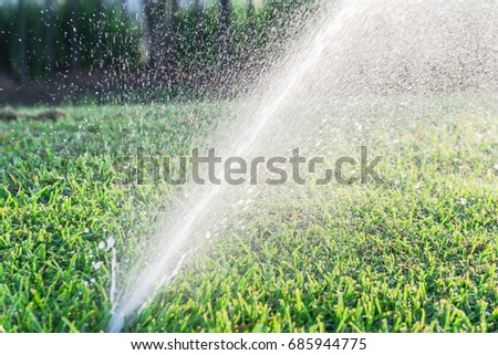 Close-up sprinklers spraying water on grass lawn irrigation at early morning. Smart garden activated with full automatic watering. Eco irrigation system, green bokeh background.