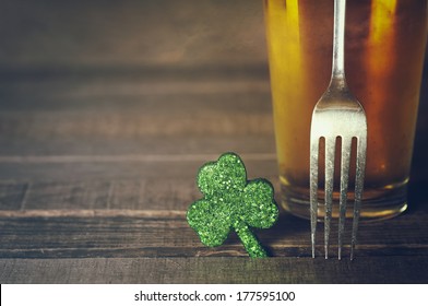 Closeup Of St. Patricks Day Green Shamrock With Fork And Frosty Cold Glass Of Beer On Wood Board Background With Room Or Space For Copy, Text, Words.  Vintage Camera Instagram Treatment For Mood