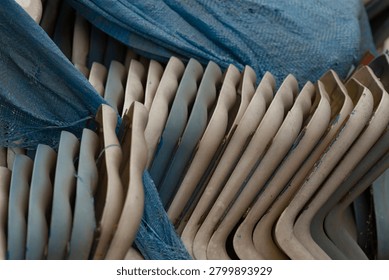 Close-up of a stack of beige plastic chairs arranged in alternating rows and partially draped with a textured blue tarp, showing scuffs, dust, and molded