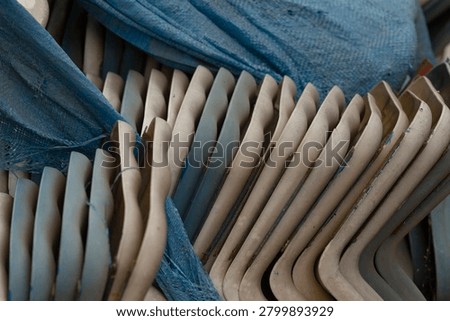 Close-up of a stack of beige plastic chairs arranged in alternating rows and partially draped with a textured blue tarp, showing scuffs, dust, and molded