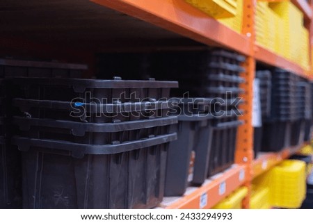Close-up stack of black tough tote made of durable recycled polypropylene with yellow reinforced snap-fit lid, lockable lid secure protect storage items at hardware store bay aisles, Dallas, TX. USA