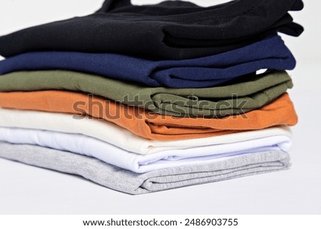 Closeup of a stack of folded blank cotton t shirts isolated over white gray background. Clothes, minimalism, retail concept.