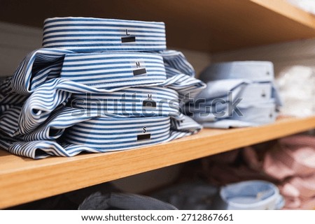 Close-up of a stack of folded blue and white striped shirts with size labels organized on a wooden shelf in a retail clothing store