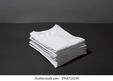 Closeup of a stack of folded white cotton t shirts isolated over dark gray background. Clothes, minimalism, retail concept. Horizontal shot