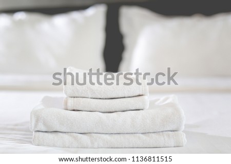 Close-up of stack of fresh white bath towels on the bed sheet. Room service maid cleaning hotel room.