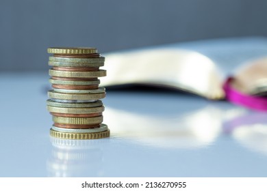 A closeup of a stack of golden coins with a Holy Bible Book in the background. The biblical concept of Christian offering, generosity, and giving tithes in church. A closeup.